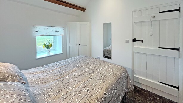Ein Schlafzimmer mit Bett, Fenster mit Blick, Kleiderschrank und Spiegel.