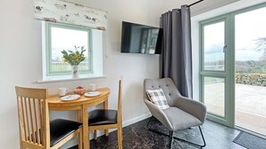 Ein Zimmer mit Esstisch, Stühlen, einem an der Wand befestigten Fernseher und Blick durch ein großes Fenster.