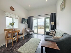 A living room with a sofa, a chair, a table, a TV, and a window with a view. - Primrose Cottage - UK51766 (Pickering)