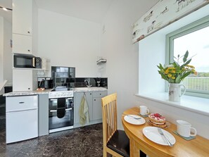A modern kitchen with a dining area, a view of the outdoors, and a window with a flower vase. - Primrose Cottage - UK51766 (Pickering)