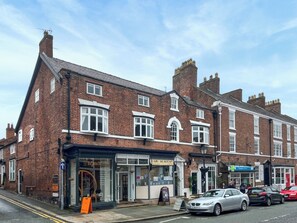 A traditional brick building with a hair salon, a pharmacy, and a sign for a hair academy. - Victoria Apartment 1 (Tarporley)