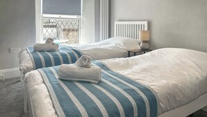 A hotel room with two beds, a window with a view, a lamp on a bedside table, and a power outlet. - 2 bedroom accommodation in St Agnes (St Agnes)