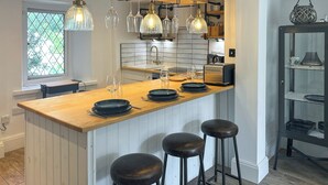 A modern kitchen with a wooden island, bar stools, pendant lights, and a view of the outdoors. - 2 bedroom accommodation in St Agnes (St Agnes)