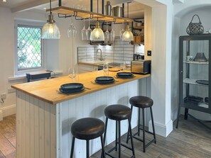 A modern kitchen with a wooden island, bar stools, pendant lights, and a view of the outdoors.