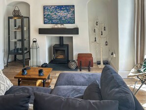 Una sala acogedora con sofá, mesa de centro, chimenea, estantería y un árbol decorativo.