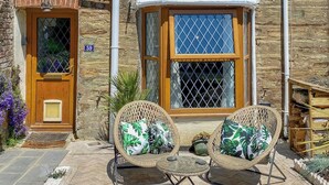 A stone building with a wooden door, a number '59' sign, a window with a white awning, and wicker chairs with cushions. - 2 bedroom accommodation in St Agnes (St Agnes)