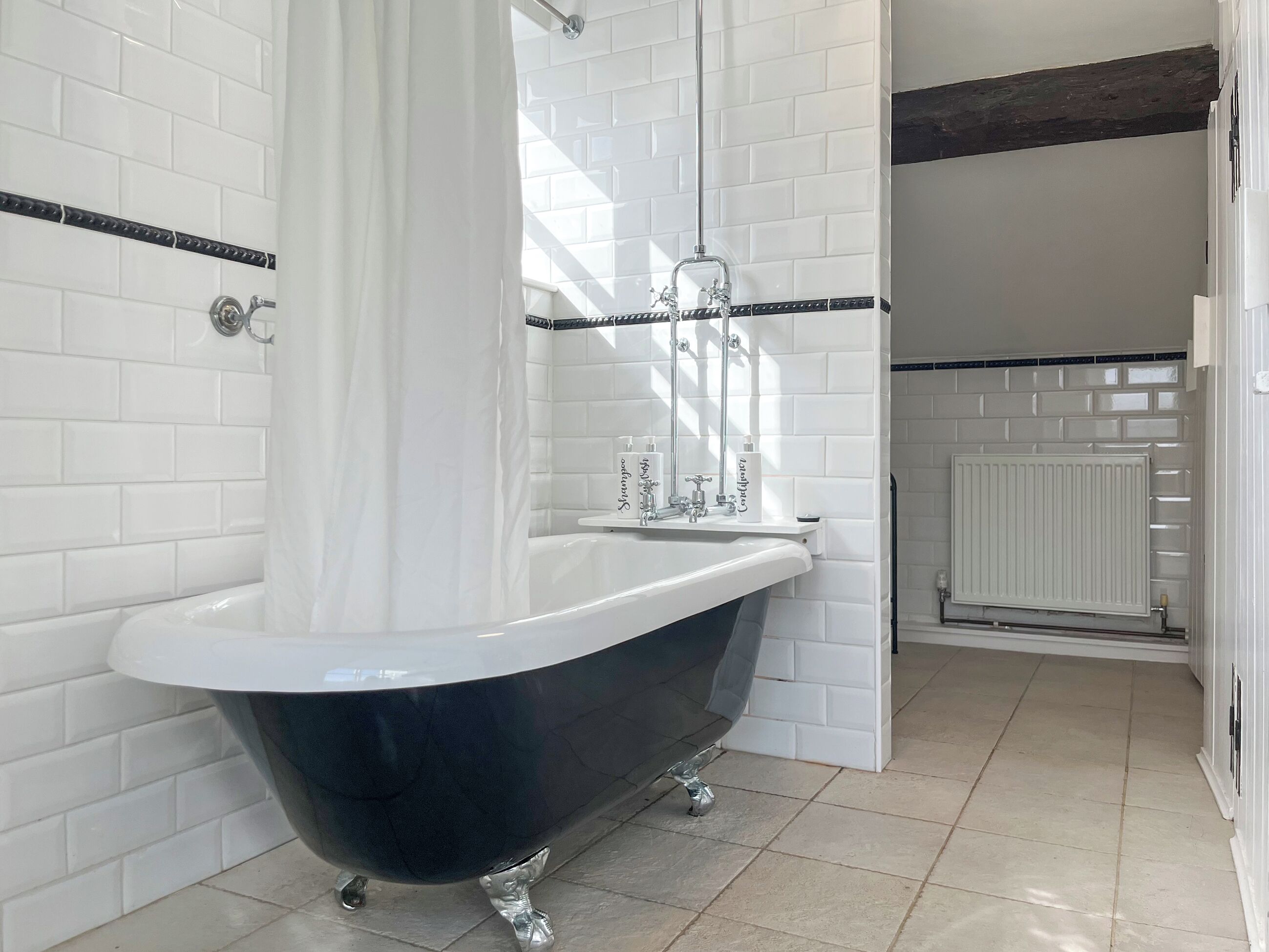 Un baño con una bañera tipo pata de león en blanco y negro, paredes de azulejos blancos y un radiador blanco.