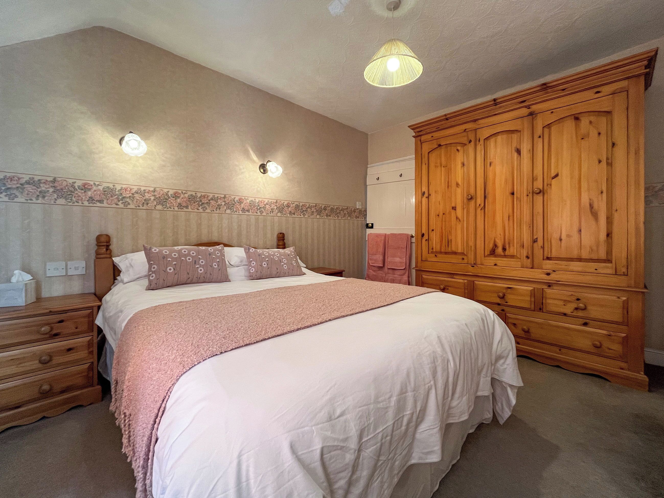 Un dormitorio con una cama grande, un armario de madera, mesitas de noche y una lámpara en el techo.