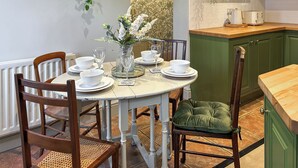 A dining area with a round table set for four, surrounded by wooden chairs, a green cushioned chair, and a vase with white flowers. - 2 bedroom accommodation in Lazonby, near Penrith (Lazonby, near Penrith)