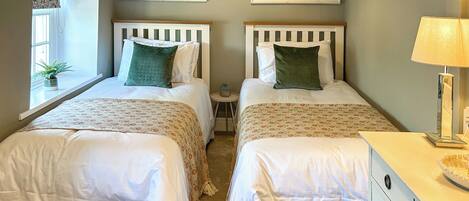 A double bed room with two beds, a small side table, a dresser, and two framed pictures on the wall.
