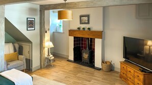 A cozy living room with a fireplace, a sofa, a television, and a lamp. - 2 bedroom accommodation in Lazonby, near Penrith (Lazonby, near Penrith)