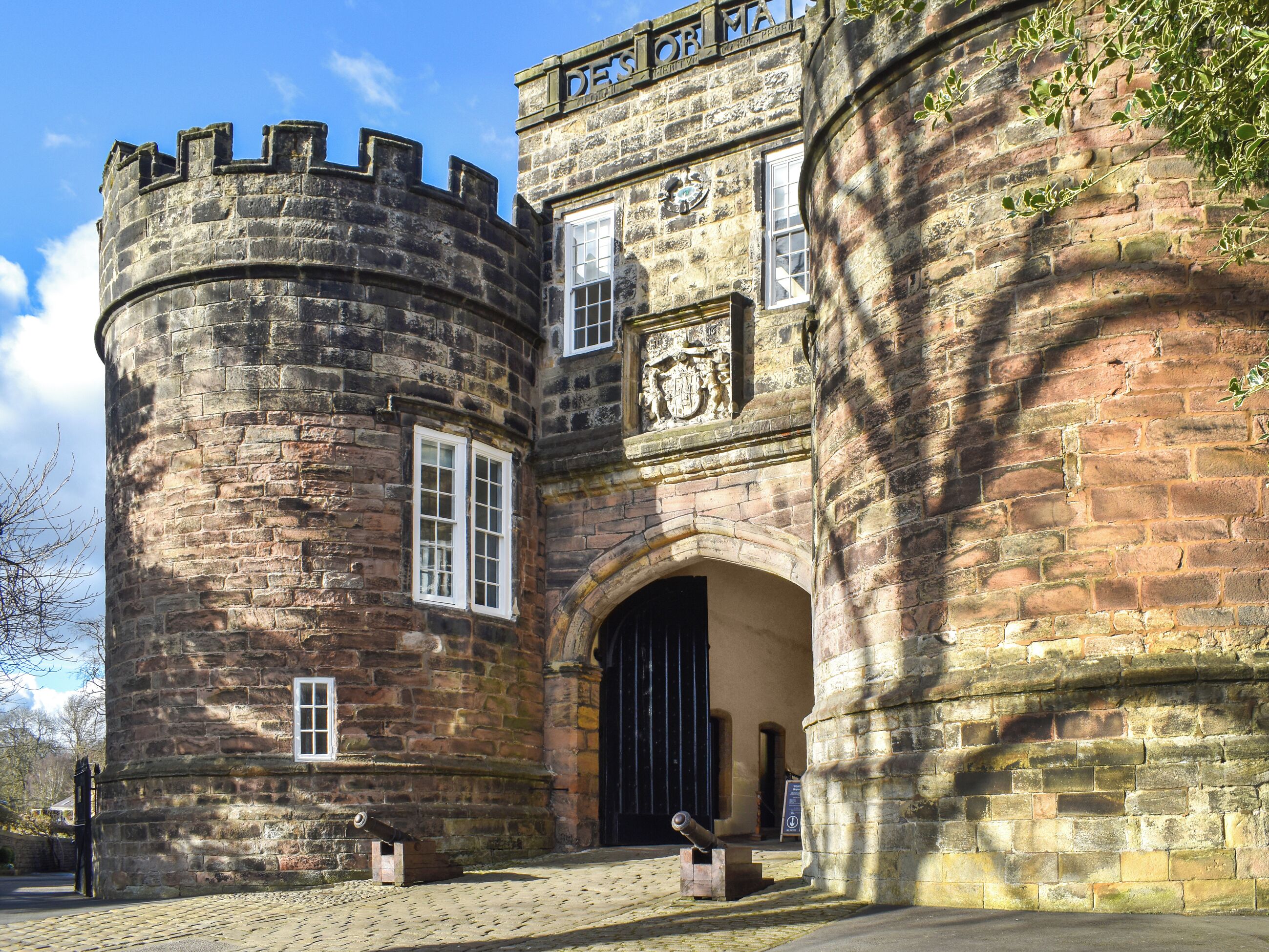 A historic stone building with a round tower, arched entrance, and a coat of arms.