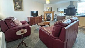 Ein Wohnzimmer mit Kamin, Fernseher und Küchenzeile.