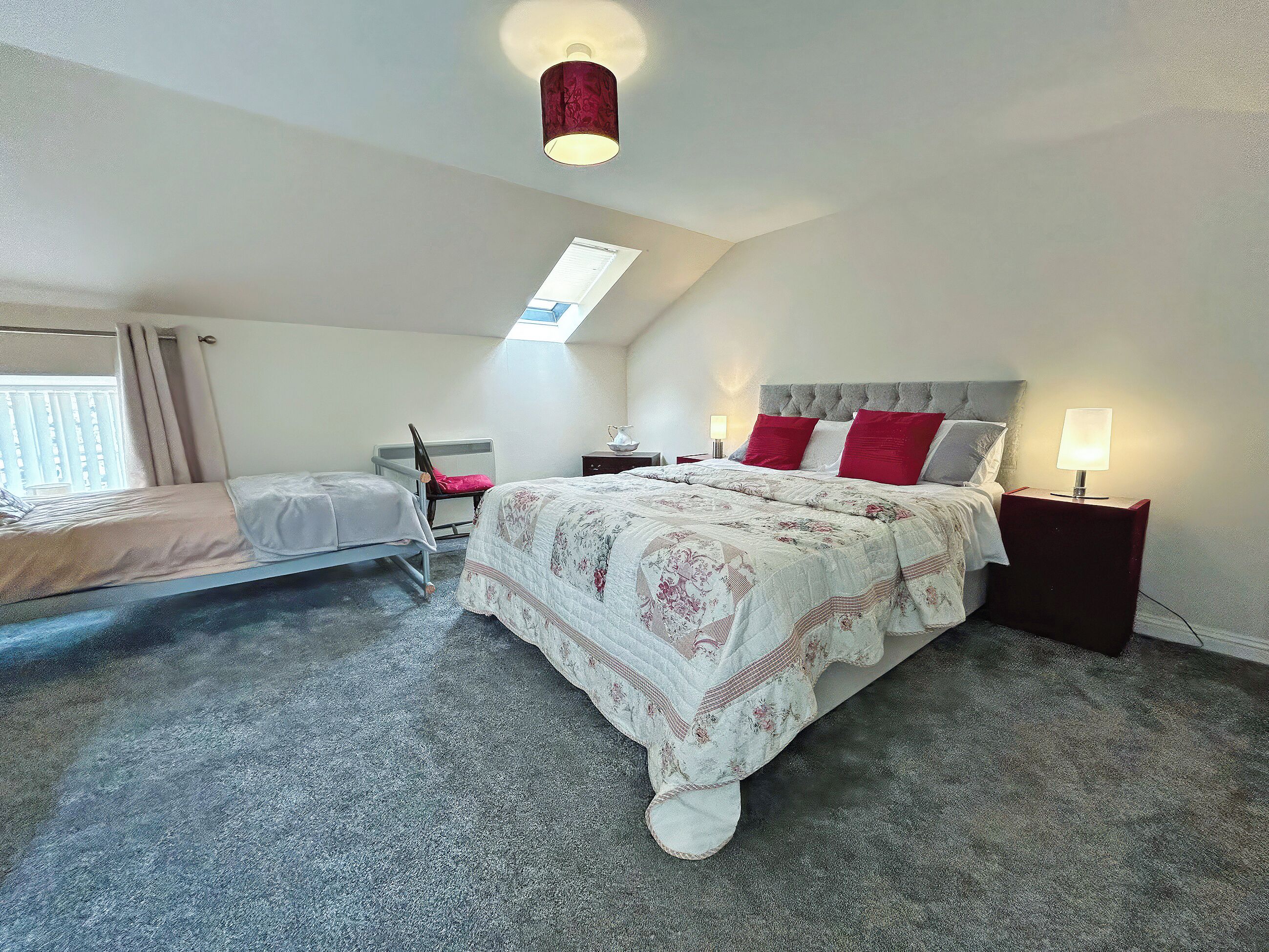 A bedroom with a large bed, a smaller bed, a chair, a nightstand, a lamp, and a ceiling light.