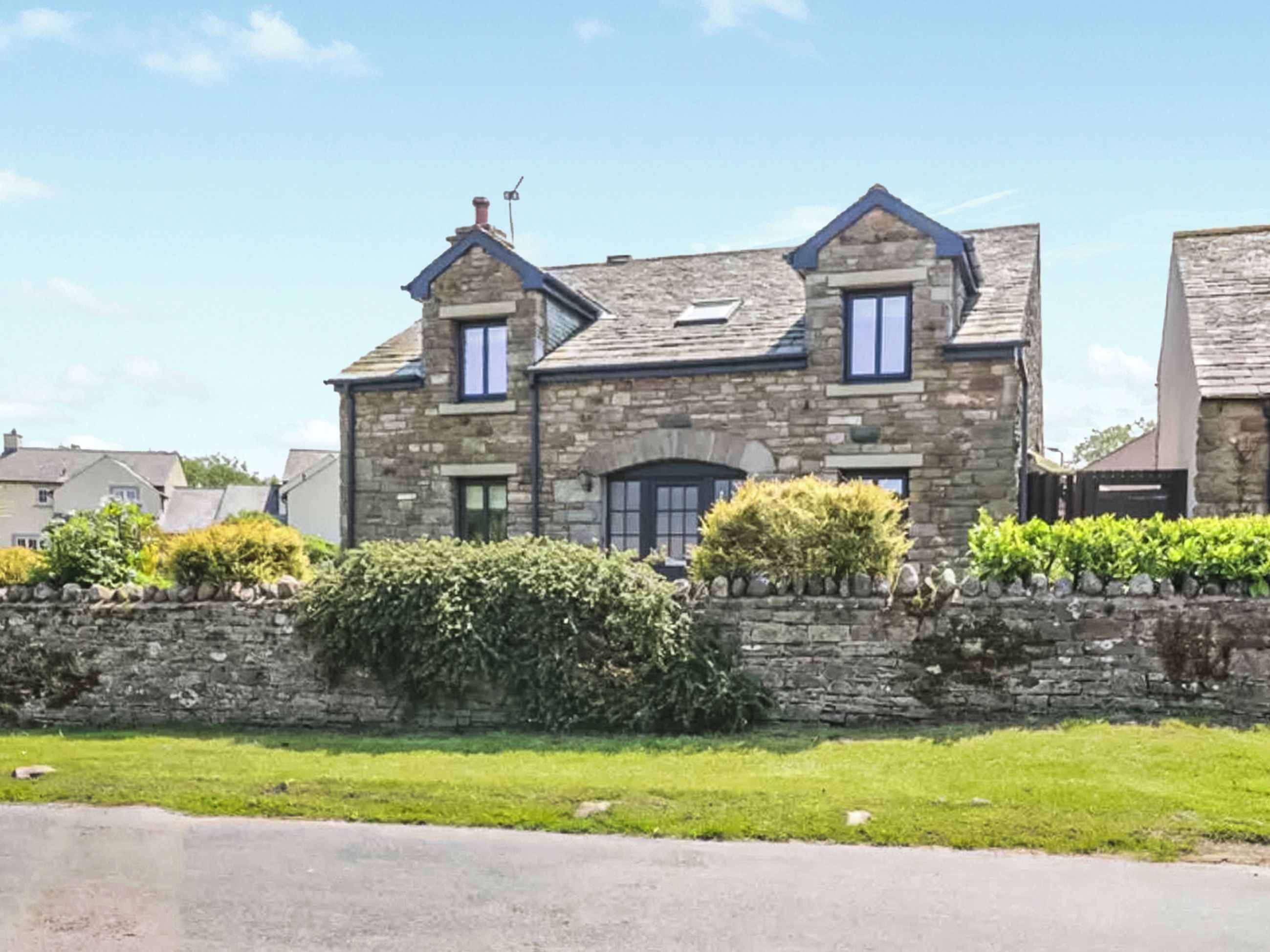 A stone house with a pitched roof, two visible windows, and a stone wall in front.