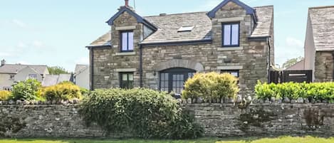 Une maison en pierre avec un toit à deux versants, deux fenêtres apparentes et un mur de pierre à l’avant.
