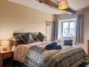 Un dormitorio con cama, almohadas, lámpara, ventana y una viga de techo de madera.