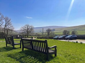 A bench in a grassy area with a view of a road and parked cars. - 3 bedroom accommodation in Halton Gill (Halton Gill)