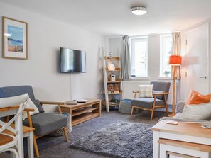 A modern living room with a flat-screen TV, a bookshelf, a grey sofa, a wooden coffee table, and a grey rug. - Strandside Townhouse (Bude)