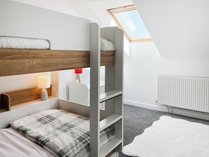 Ein Etagenbett mit Holzkopfende, einer Nachttischlampe, einem Heizkörper und einem Dachfenster.