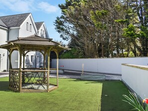 A gazebo with a lattice design, a lawn, and a white wall with a low fence. - Strandside Townhouse (Bude)