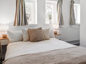 A bedroom with a large bed, two bedside tables, a window with curtains, and a radiator. - Strandside Townhouse (Bude)