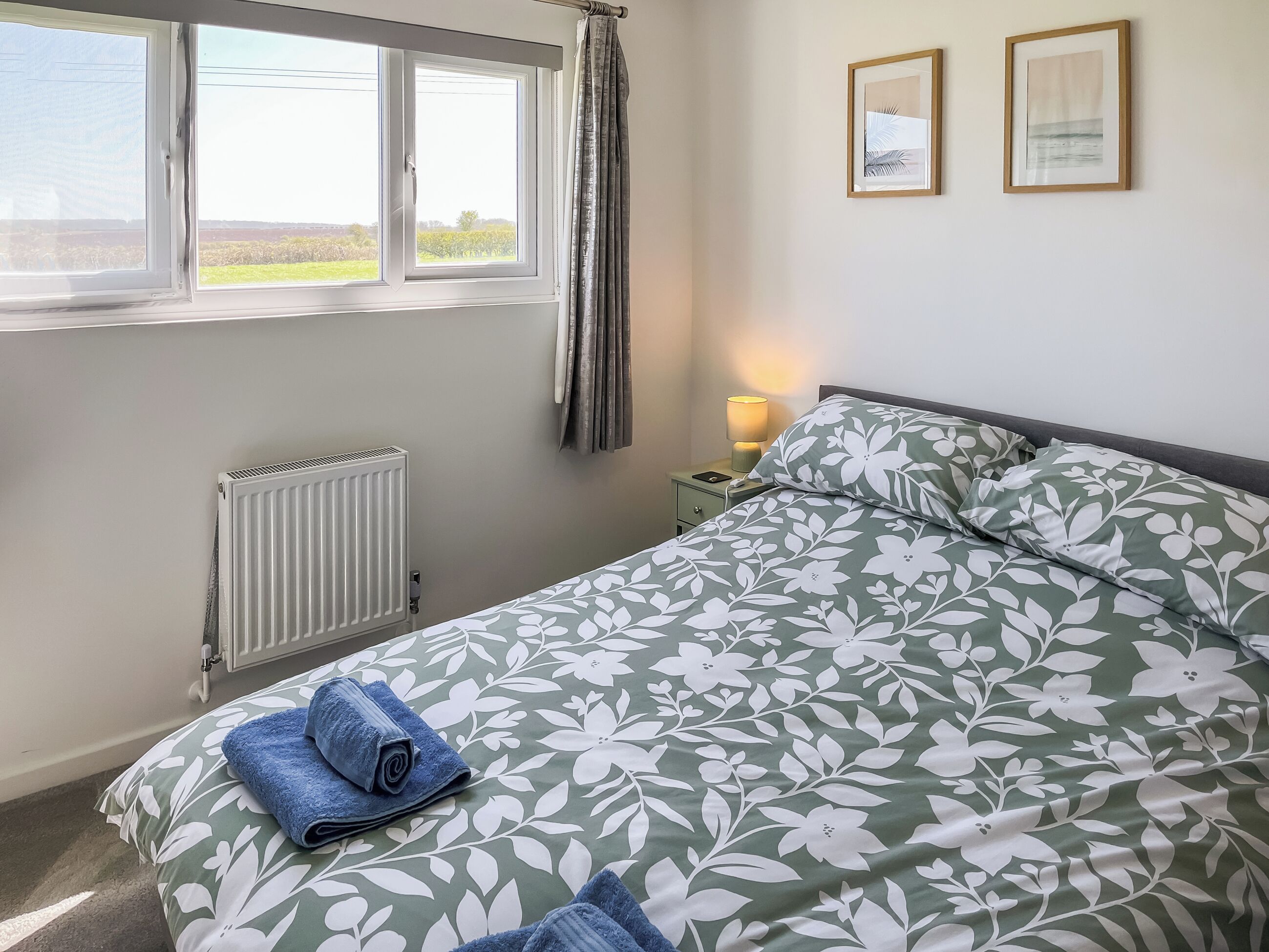 Een slaapkamer met een bed, een radiator, een nachtkastje met een lamp en een raam met gordijnen.