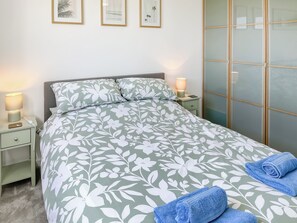 Una cama bien hecha con ropa de cama floral, una lámpara de noche y una toalla doblada al lado.