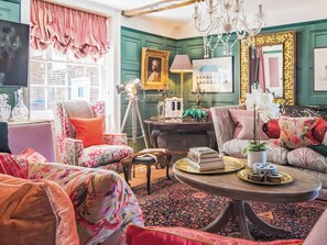 A room with a green wall, a chandelier, a sofa, a chair, a table with books, and a window with curtains. - 6 bedroom accommodation in Sandwich (Sandwich)