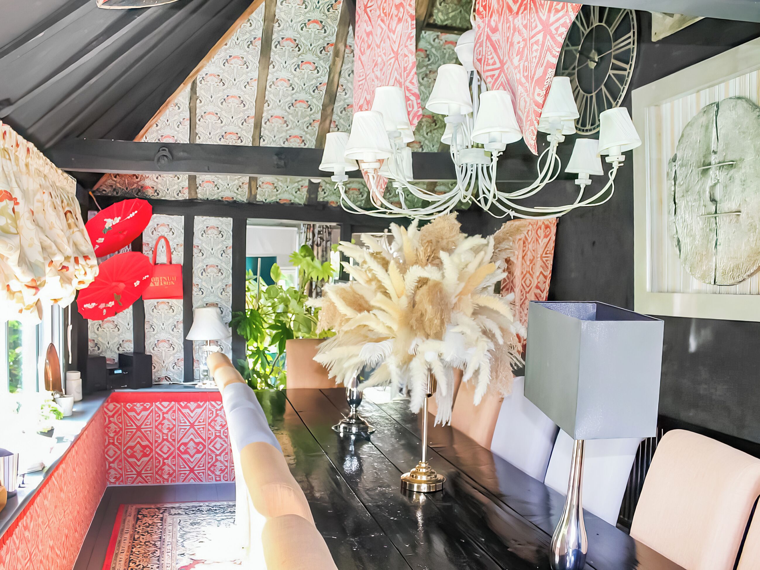 Un comedor con una mesa de madera oscura, sillas blancas, una araña y papel tapiz estampado.