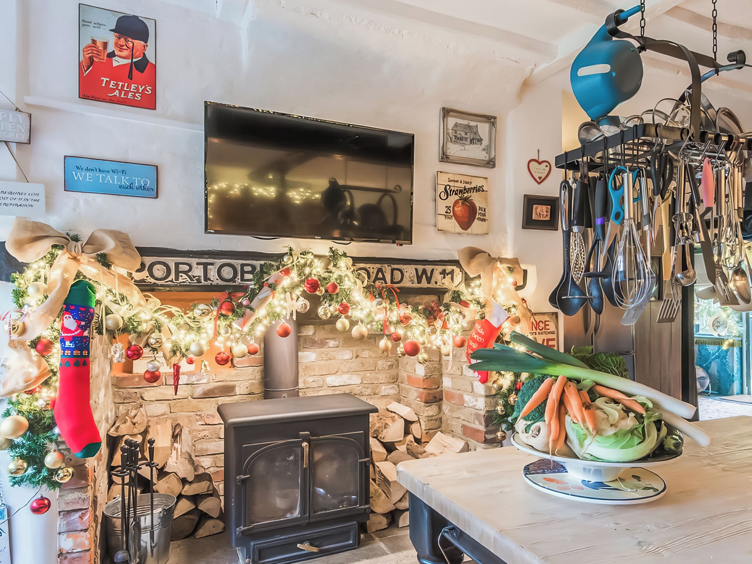 A cozy room with a fireplace, a television, and a kitchen area with utensils hanging above.