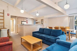 A modern living room with a sofa, a wooden coffee table, and a dining area with chairs and a table.