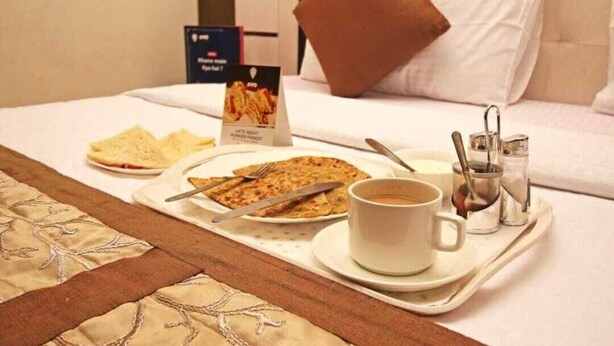Un plat de petit esmorzar ben organitzat damunt un llit, amb un almoiner, una tassa de cafè i un plat de menjar.