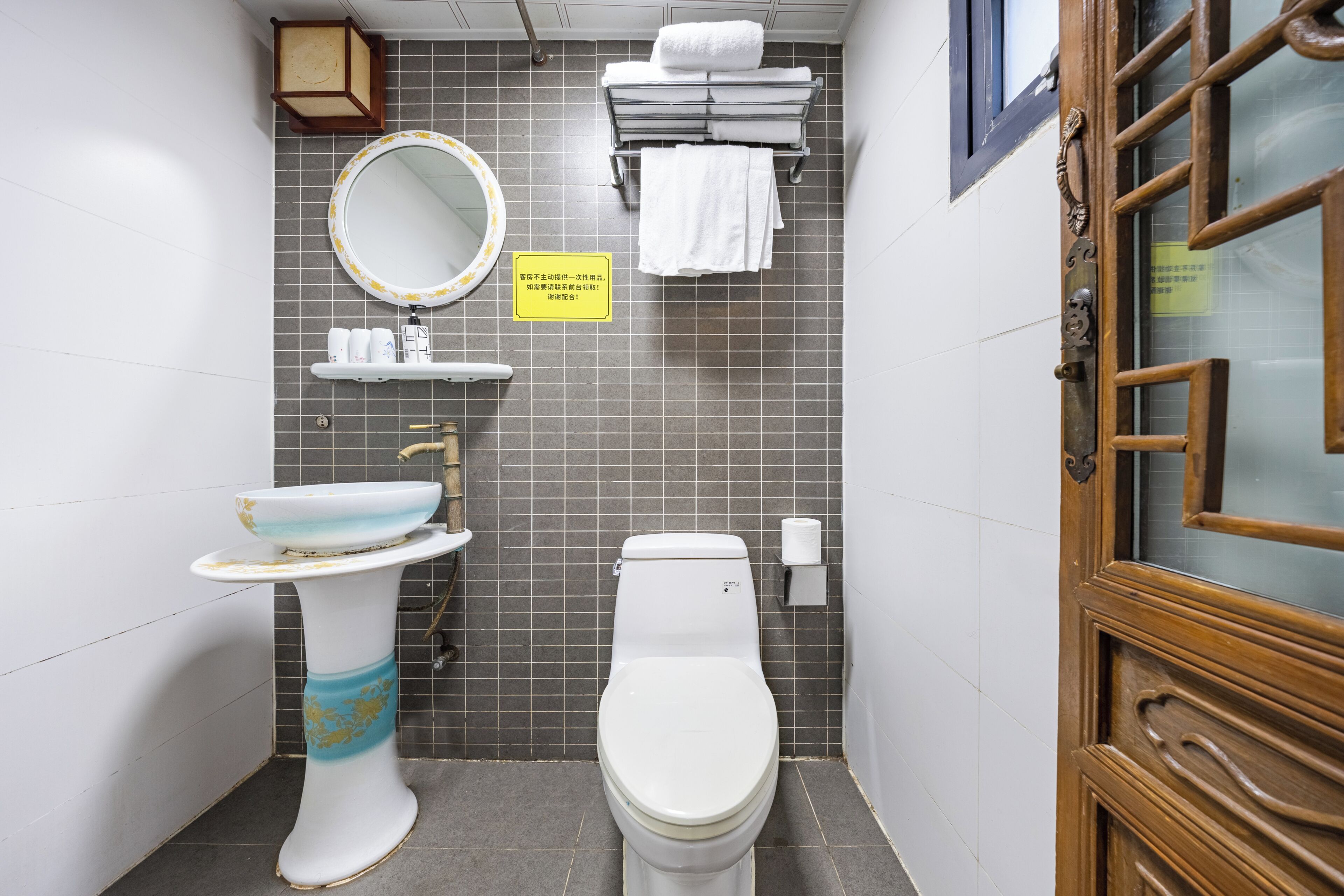 A compact bathroom with a toilet, sink, and mirror. There are towels and toiletries on the wall.