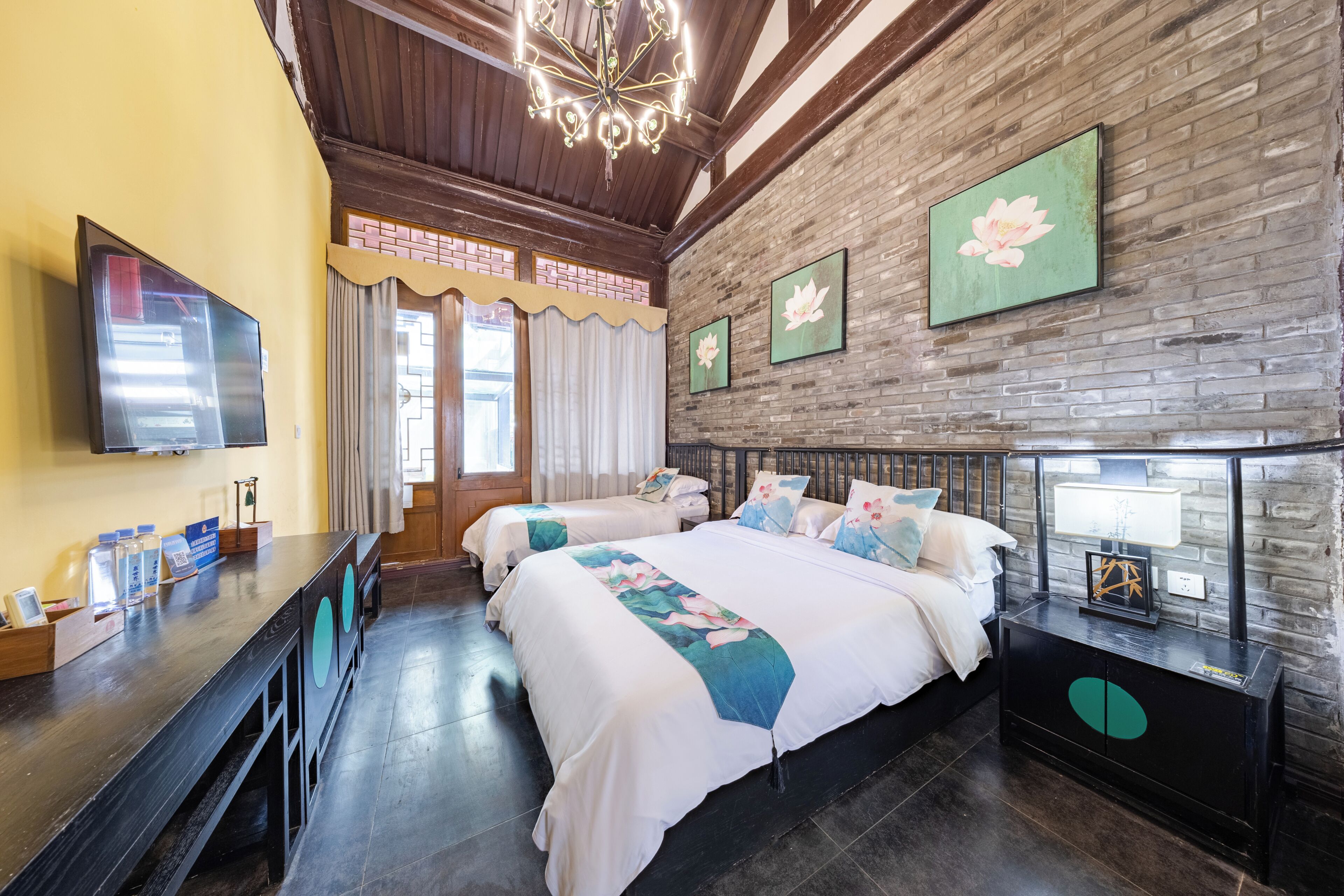 Een hotelkamer met een bakstenen muur, een groot bed met bloemenbedrukking, een bureau met een flatscreen-televisie en een nachtkastje met een lamp.