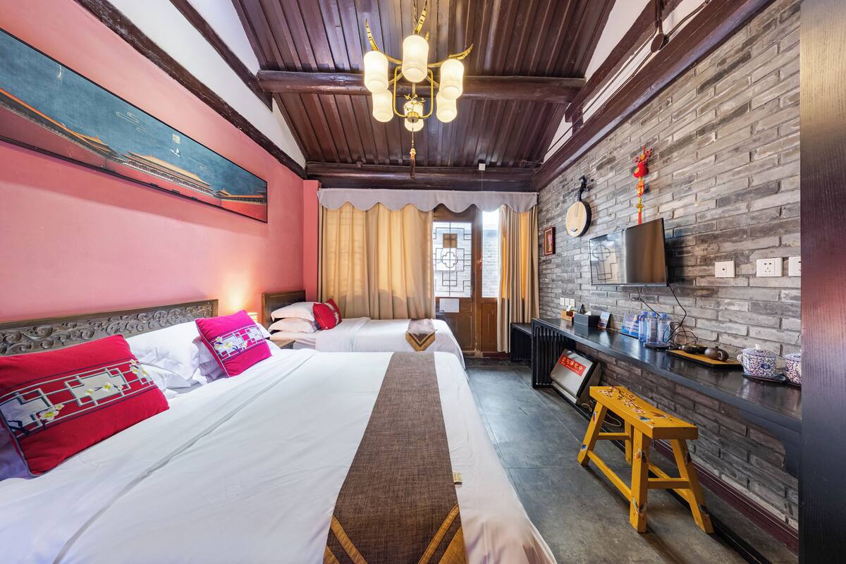 Ein Hotelzimmer mit zwei Betten, Holzboden, Backsteinwand, Fernseher und einem kleinen Hocker.