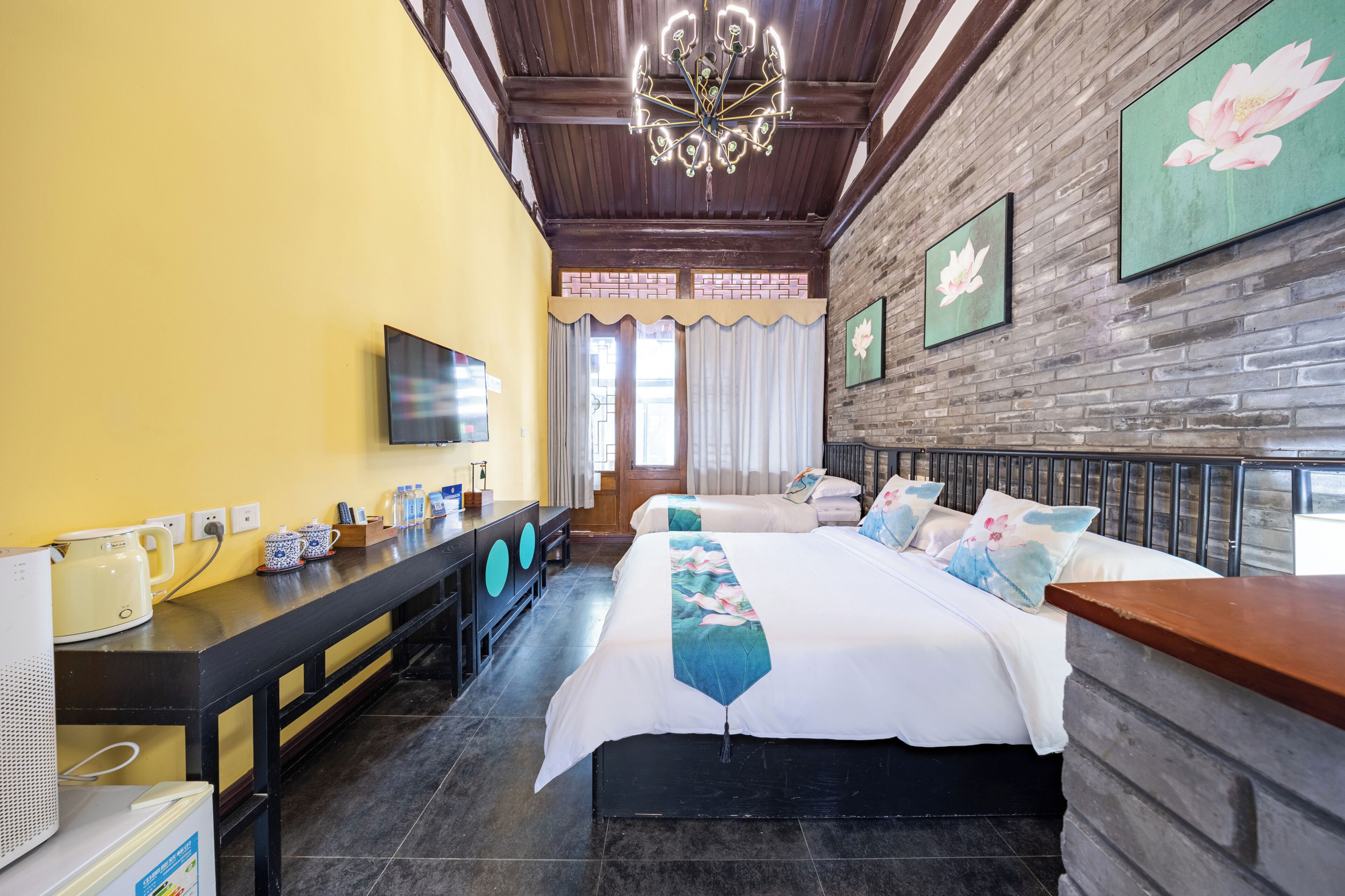 A hotel room with a bed, a TV, a desk with a kettle, and a brick wall.