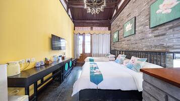 A hotel room with a bed, a TV, a desk with a kettle, and a brick wall.