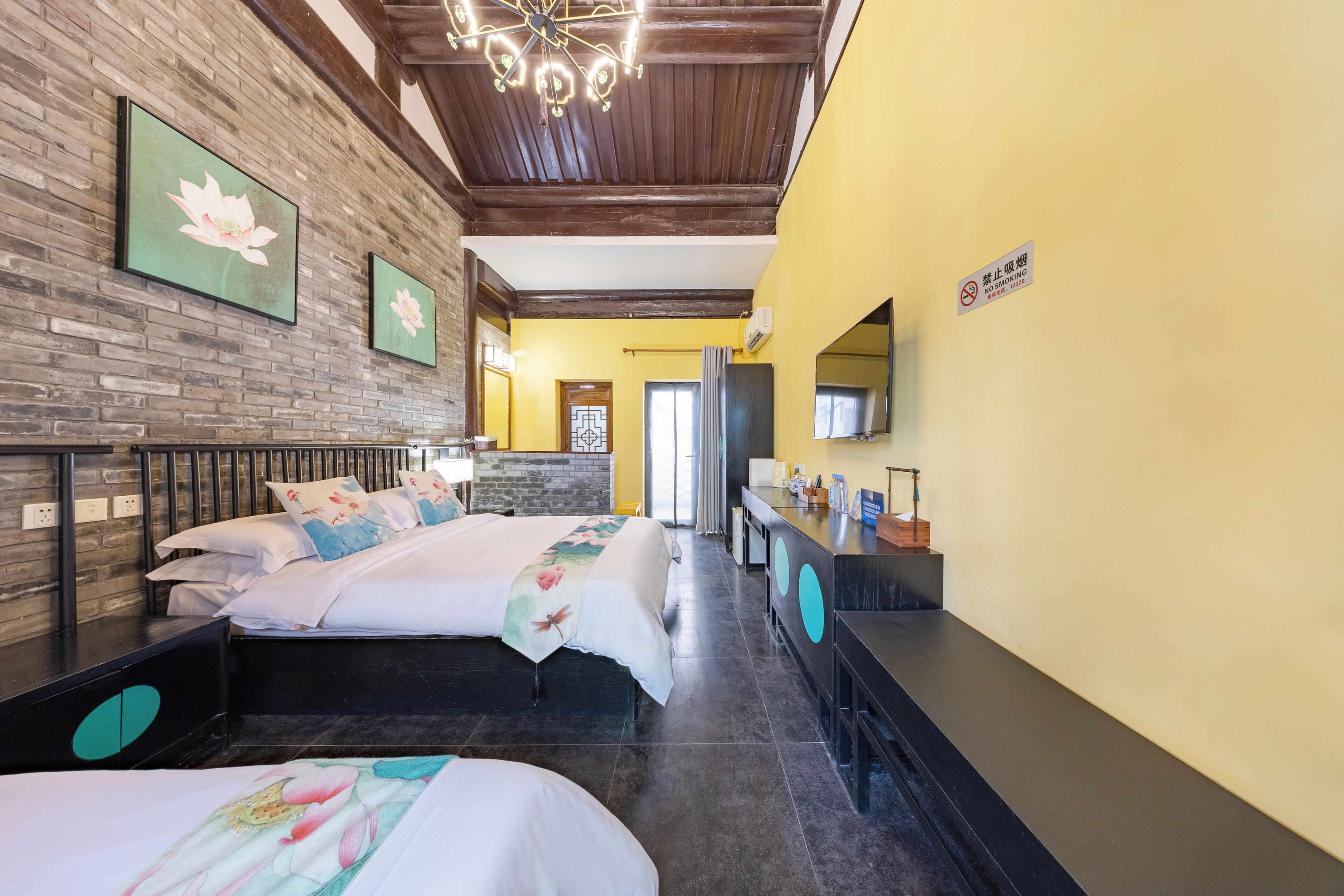 Habitación de hotel con dos camas, una pared de ladrillo, techo de madera y pared amarilla.