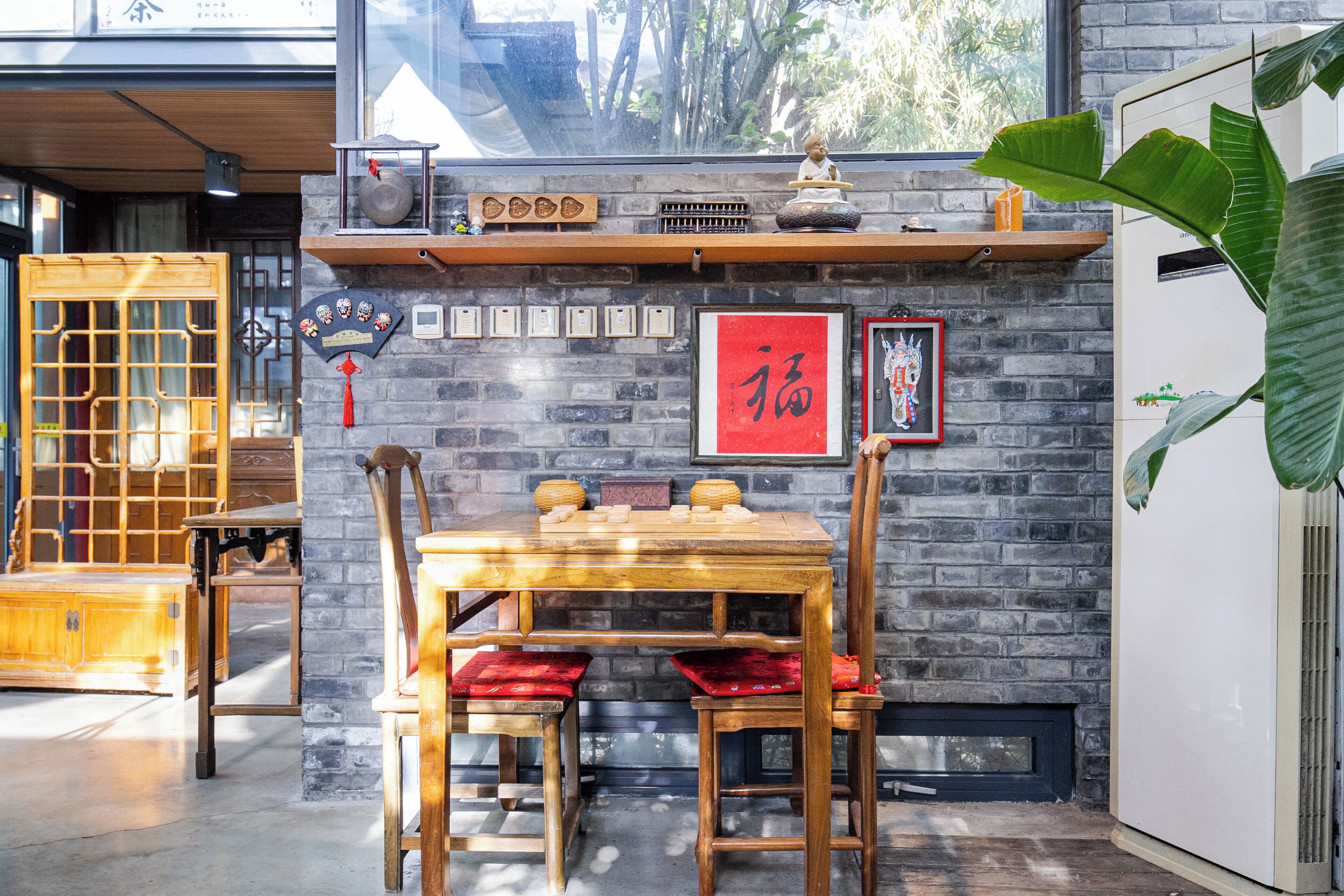 A traditional wooden dining table with chairs, a brick wall with decorative items, and a large plant.