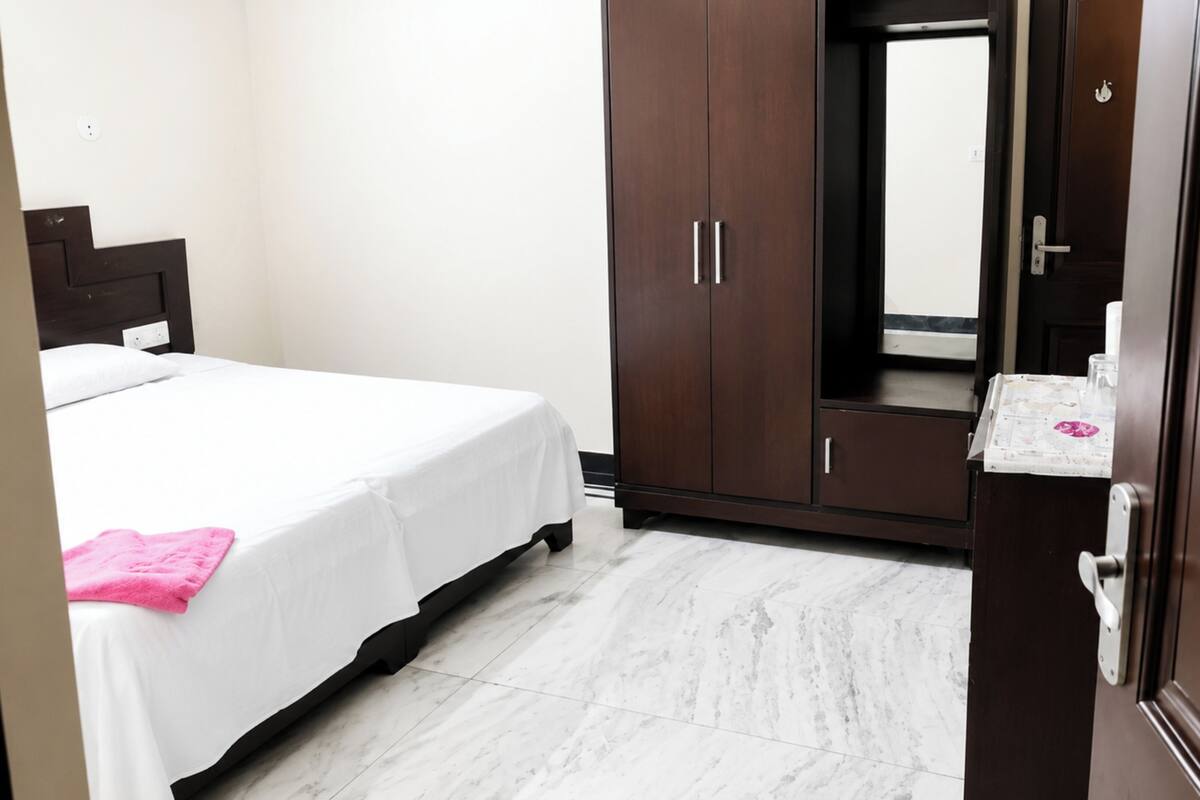 A hotel room with a bed, a wardrobe, a mirror, and a small table with toiletries.