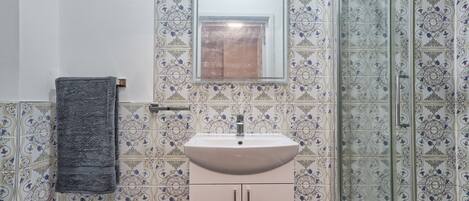 A bathroom with patterned tiles, a sink, a mirror, and a towel rack.