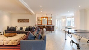 A spacious living room with a sofa, a ping pong table, and a kitchen area with a bar.