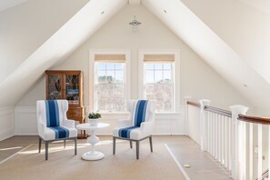 A room with a high ceiling, two chairs with blue stripes, a small round table, a wooden cabinet, and a view through two windows. - 8BR Pondfront Estate with Ocean Views, Pool, Spa, Tennis and Golf Club Access (Nantucket)