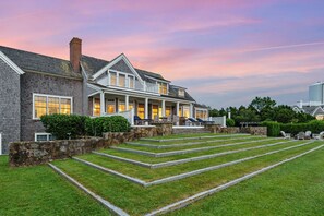 A two-story house with a stone staircase leading to a porch, surrounded by a well-maintained lawn.
