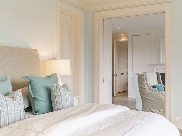 A hotel room with a large bed, a sitting area with a chair, and a door leading to another room.