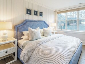 Un dormitorio con una cama, dos mesitas de noche, un ventanal y decoración de paredes temática náutica.