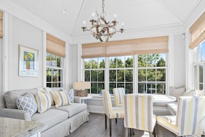 A sunroom with a sofa, chairs, a table, and a chandelier.