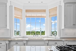 A kitchen with a large window, white cabinetry, and a gas stove.