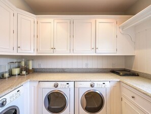 A laundry room with two front-loading washing machines, white cabinetry, and a granite countertop.